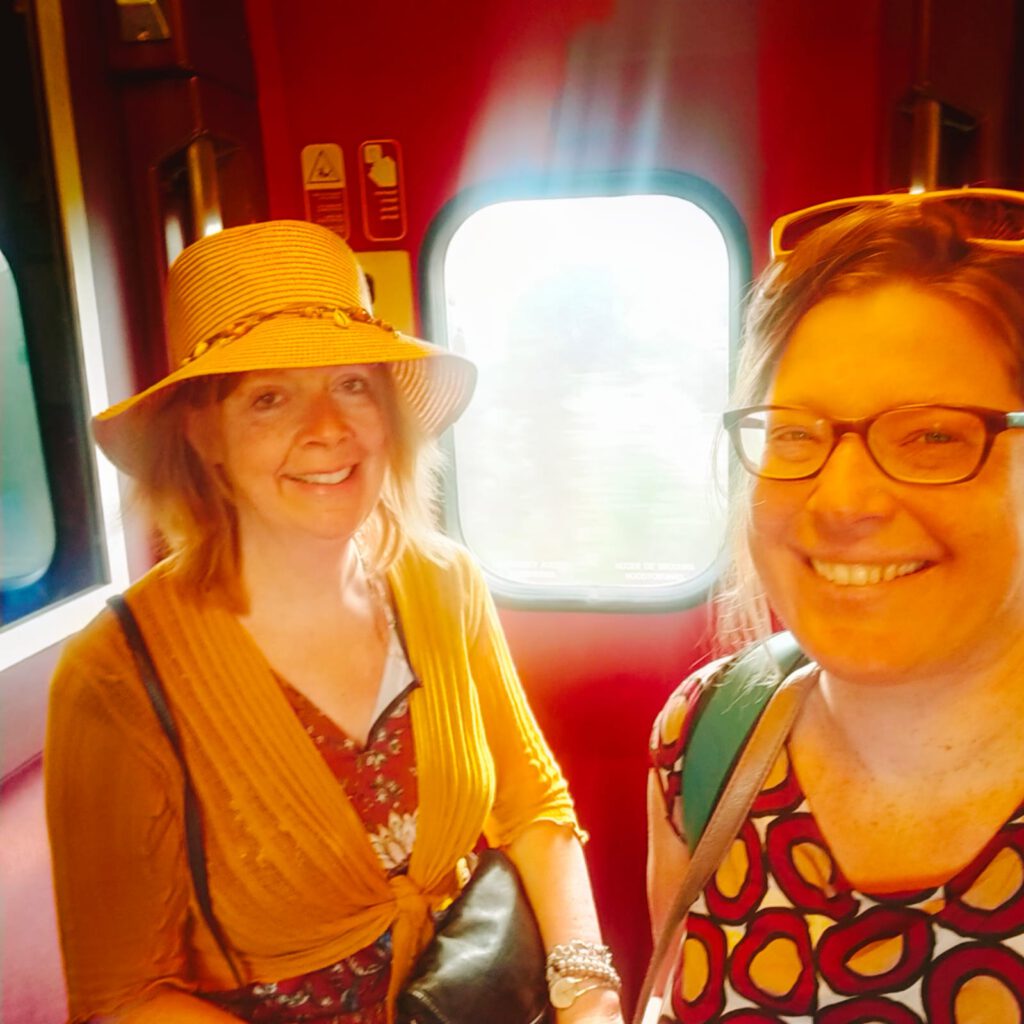 Olga met hoed, Anneke met zonnebril in de trein bij het raam