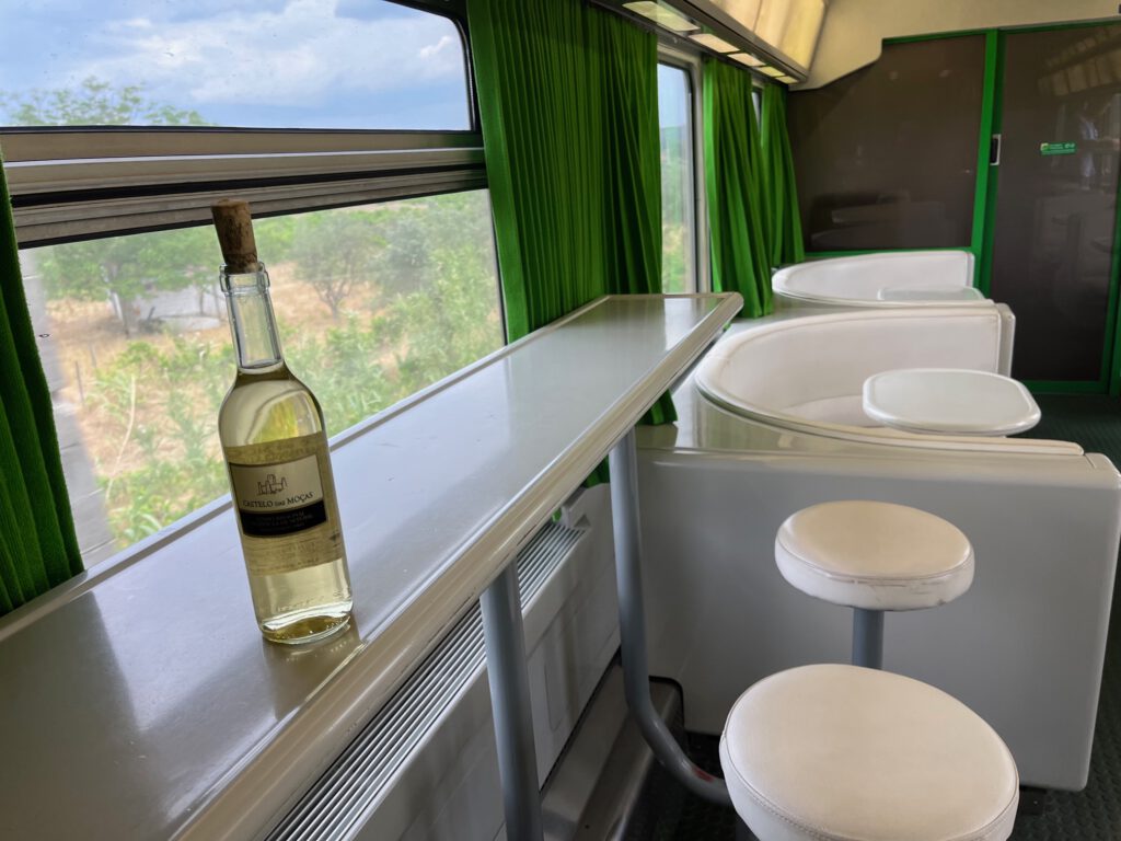 wit barretje met witgelakte barkrukken, groene gordijnen voor de ramen en een flesje witte wijn met kun dat klaarstaan op de bar